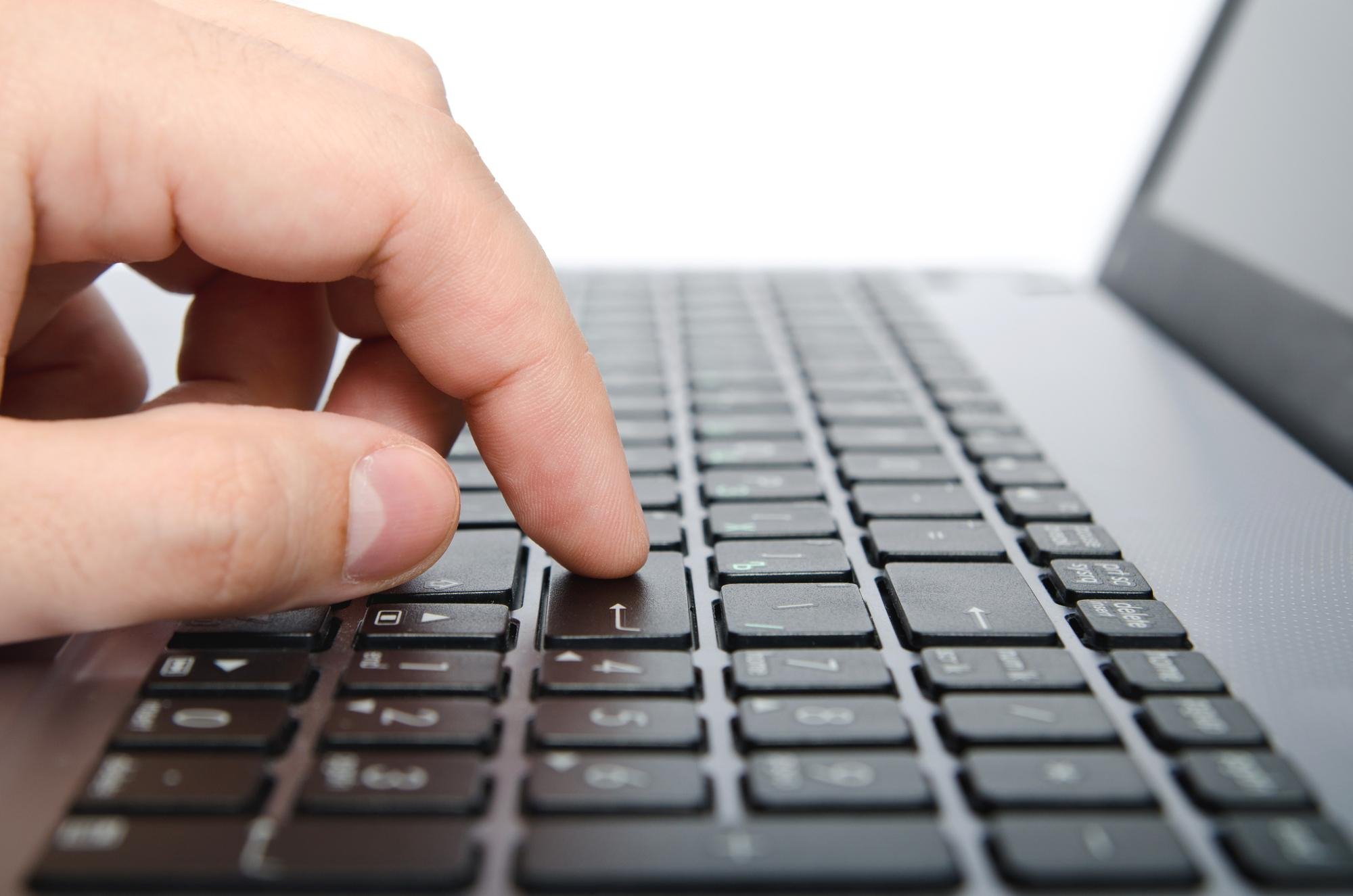 Una mano che preme il tasto Invio su una tastiera di laptop.